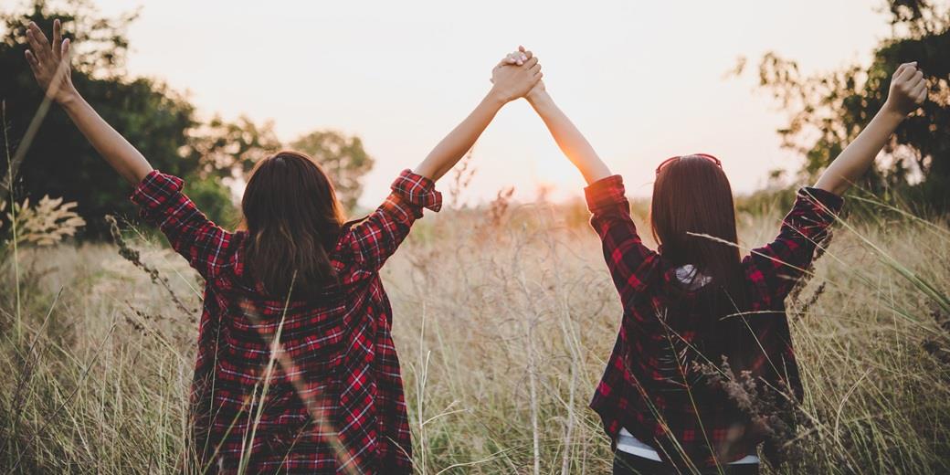 Two persons holding hands in celebration looking at sundown